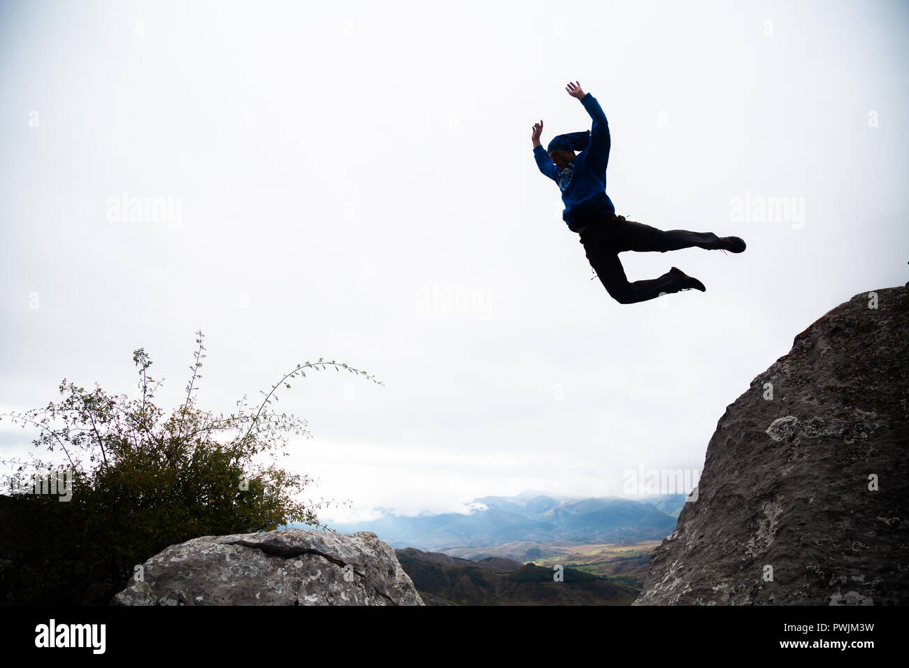 Da sotto vista di uomo sportivo saltando di roccia in roccia facendo parkour nel pomeriggio. Foto Stock