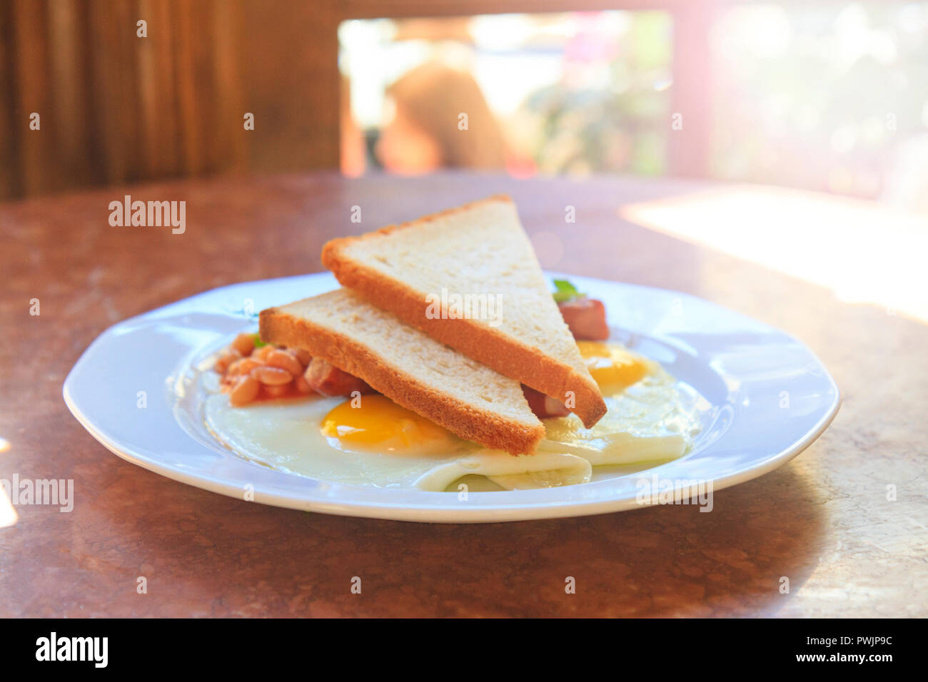 Uovo con fagioli e toast su una piastra bianca con hotspot soleggiato Foto Stock