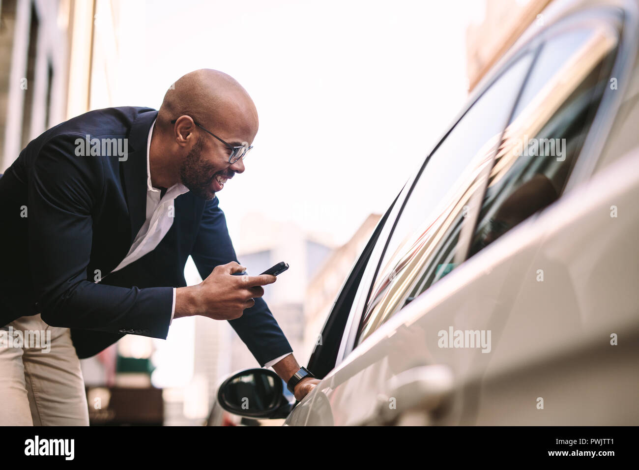 Imprenditore sorridente con telefono a parlare su taxi driver in auto. Parlando di passeggeri con autista di taxi sulla strada. Foto Stock
