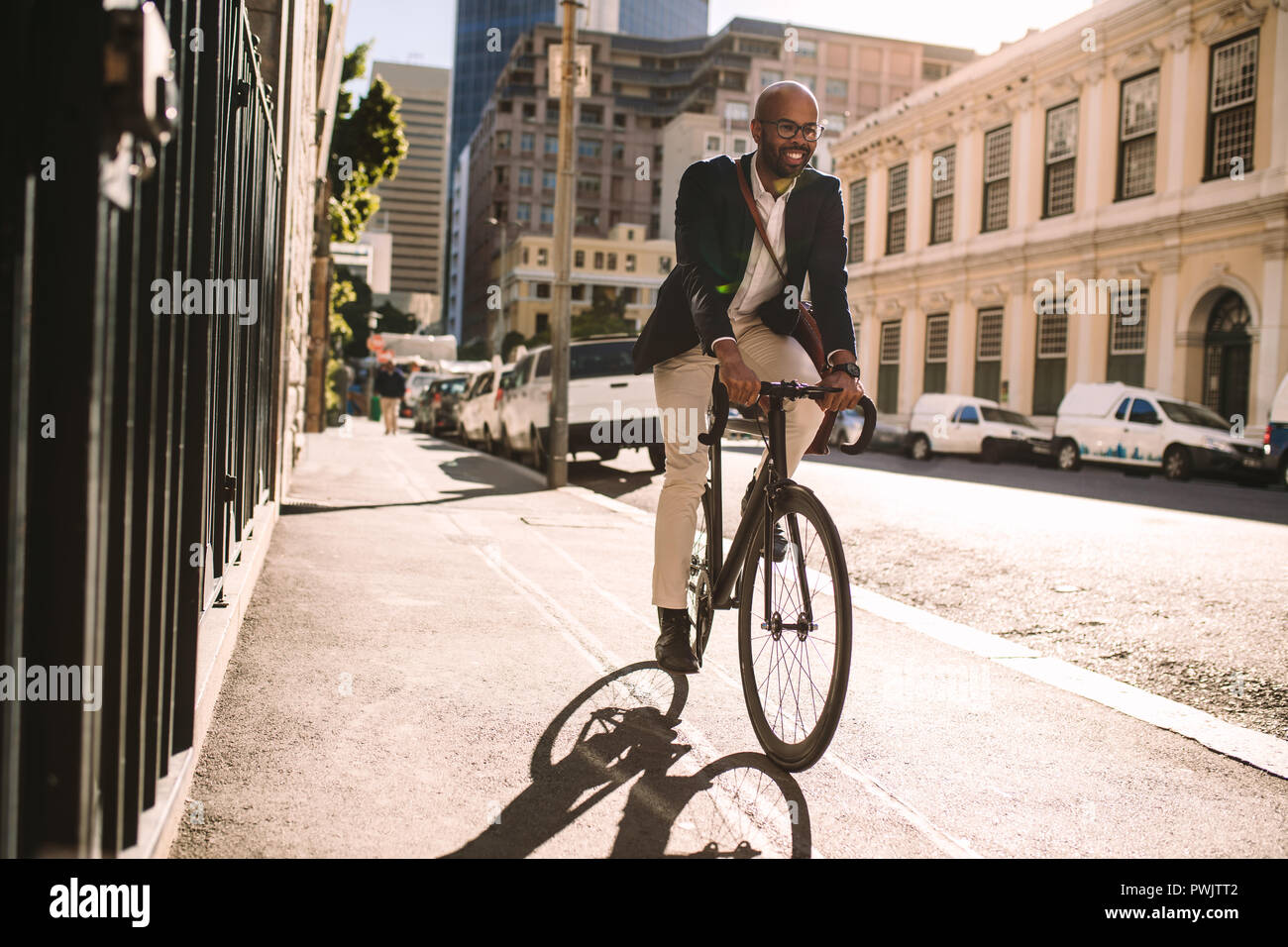 Giovane imprenditore sorridente di andare al lavoro in bicicletta. Uomo in tuta equitazione Bicicletta sul marciapiede in mattina. Foto Stock