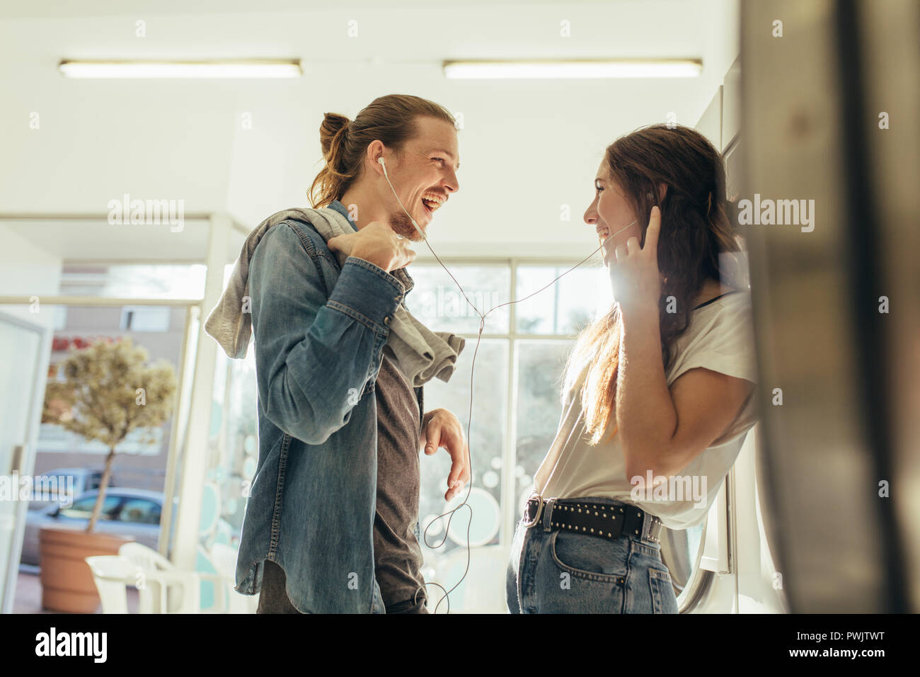 La condivisione di coppia di auricolari per ascoltare musica in piedi a casa. Matura in amore divertirsi ascoltando musica in piedi in lavanderia. Foto Stock