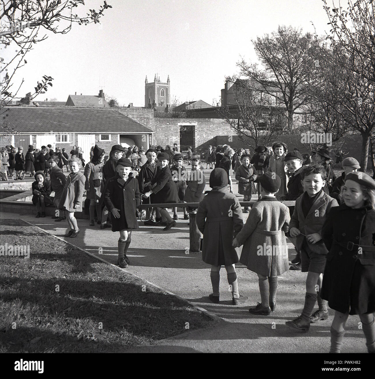 Degli anni Cinquanta, storico, istruzione, aria fresca a break-tempo, i bambini in cappotti e cappelli fuori nel parco giochi presso un villaggio inglese scuola primaria, Engalnd, UK. Foto Stock