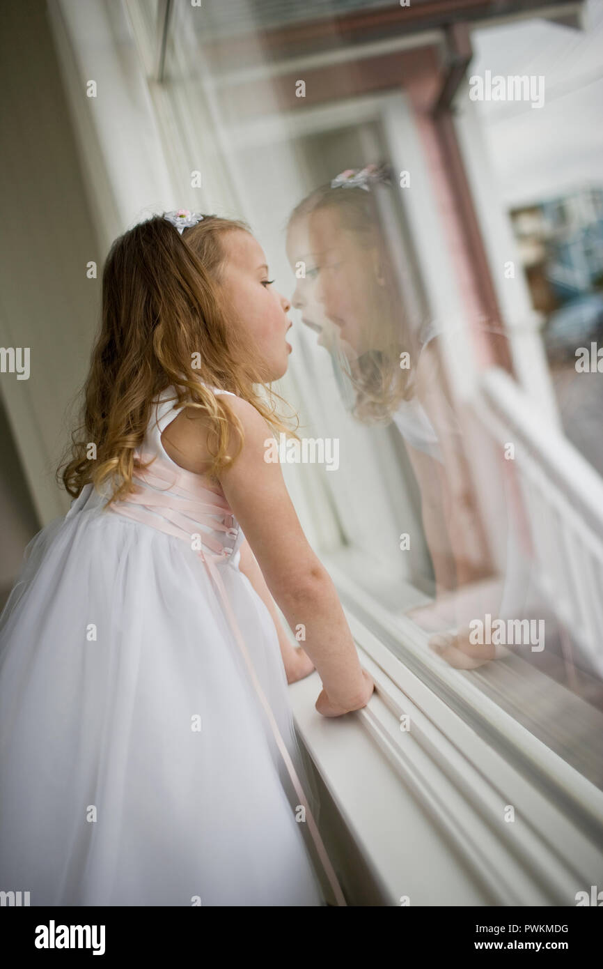 Giovane ragazza sta in piedi in una finestra vestito come un flowergirl. Foto Stock