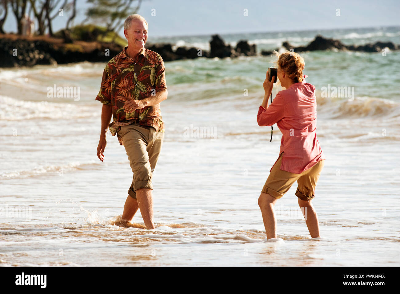 Coppia sulla spiaggia scherzosamente prendendo le foto di ogni altro. Foto Stock