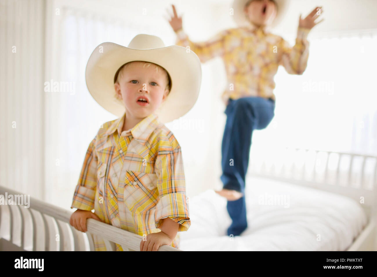 Ritratto di un giovane ragazzo che indossa un cappello mentre in piedi su un letto con il suo fratello più anziano. Foto Stock