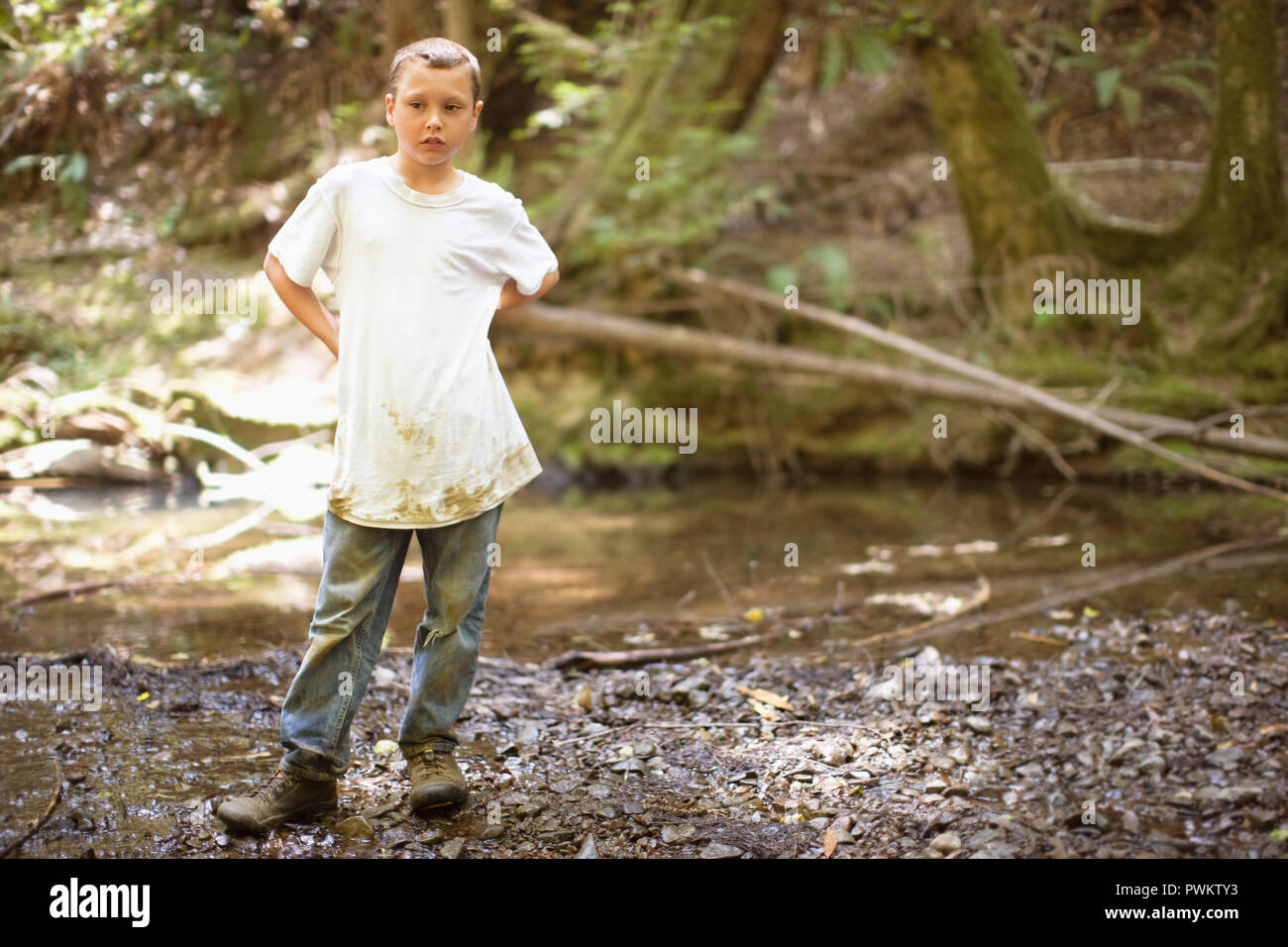 Ragazzo in piedi in una foresta indossando vestiti sporchi. Foto Stock