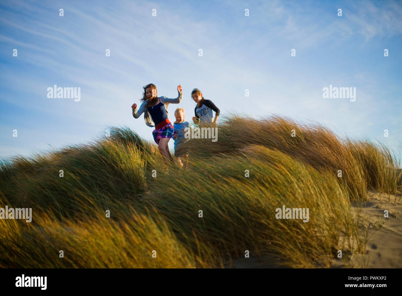 Tre bambini felicemente funzionare giù un grassy duna di sabbia. Foto Stock