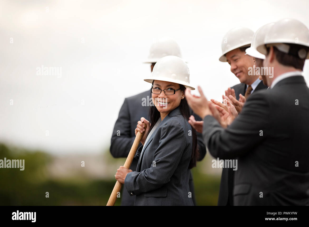 Sorridente di mezza età imprenditrice esegue la cerimonia innovativa di un nuovo sviluppo come i suoi colleghi guardano su felicemente e applaudire. Foto Stock