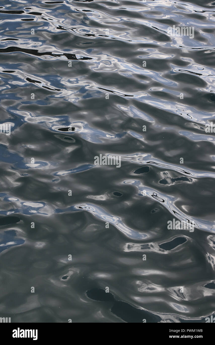 Full-frame abstract di dolci onde sulla superficie del mare come visto da sopra e con un sacco di riflessioni di cielo blu e nuvole bianche; buona per lo sfondo. Foto Stock