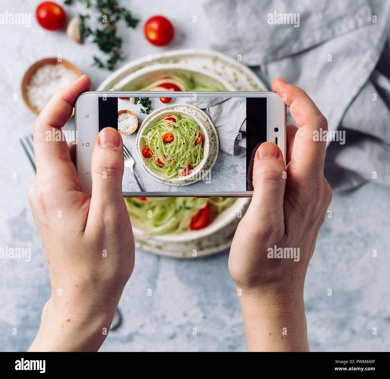 La donna tiene le mani in alto consente di visualizzare la fotografia di zucchine insalata di tagliatelle sul tavolo con telefono. Foto dello smartphone per le reti sociali o blog post.vegetariano, sano, organico, pulire, mangiare cibo crudo concetto Foto Stock