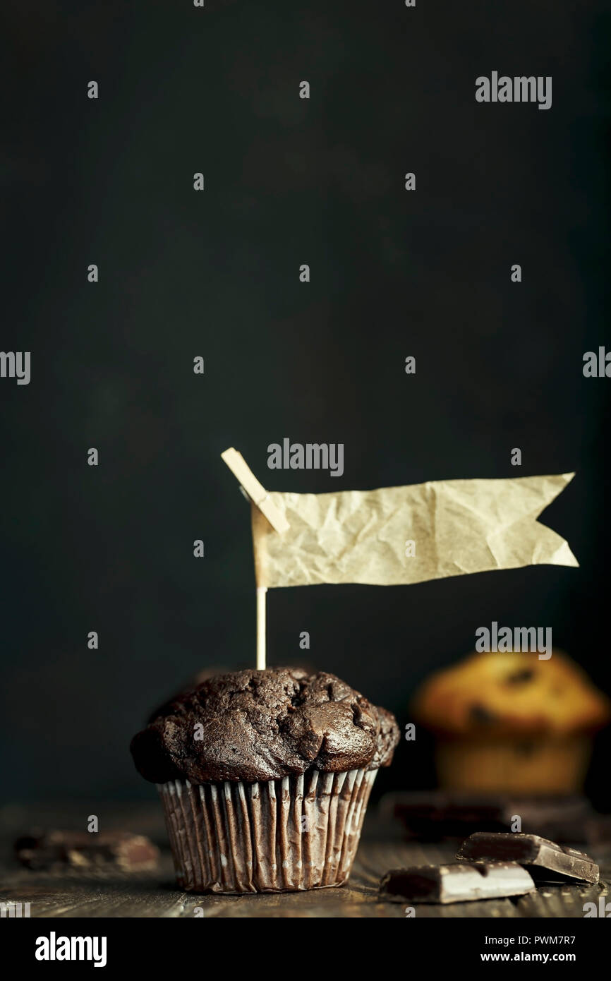 Muffin al cioccolato con bandiere di carta contro uno sfondo scuro Foto Stock