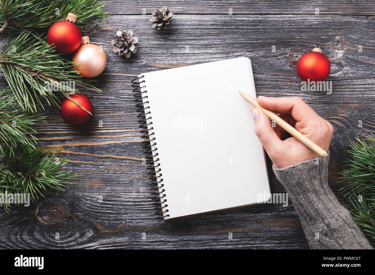 Mockup con carta bianca notebook e le decorazioni di Natale sulla tavola di legno. La donna è la scrittura a mano in notepad. Vista dall'alto. Foto Stock