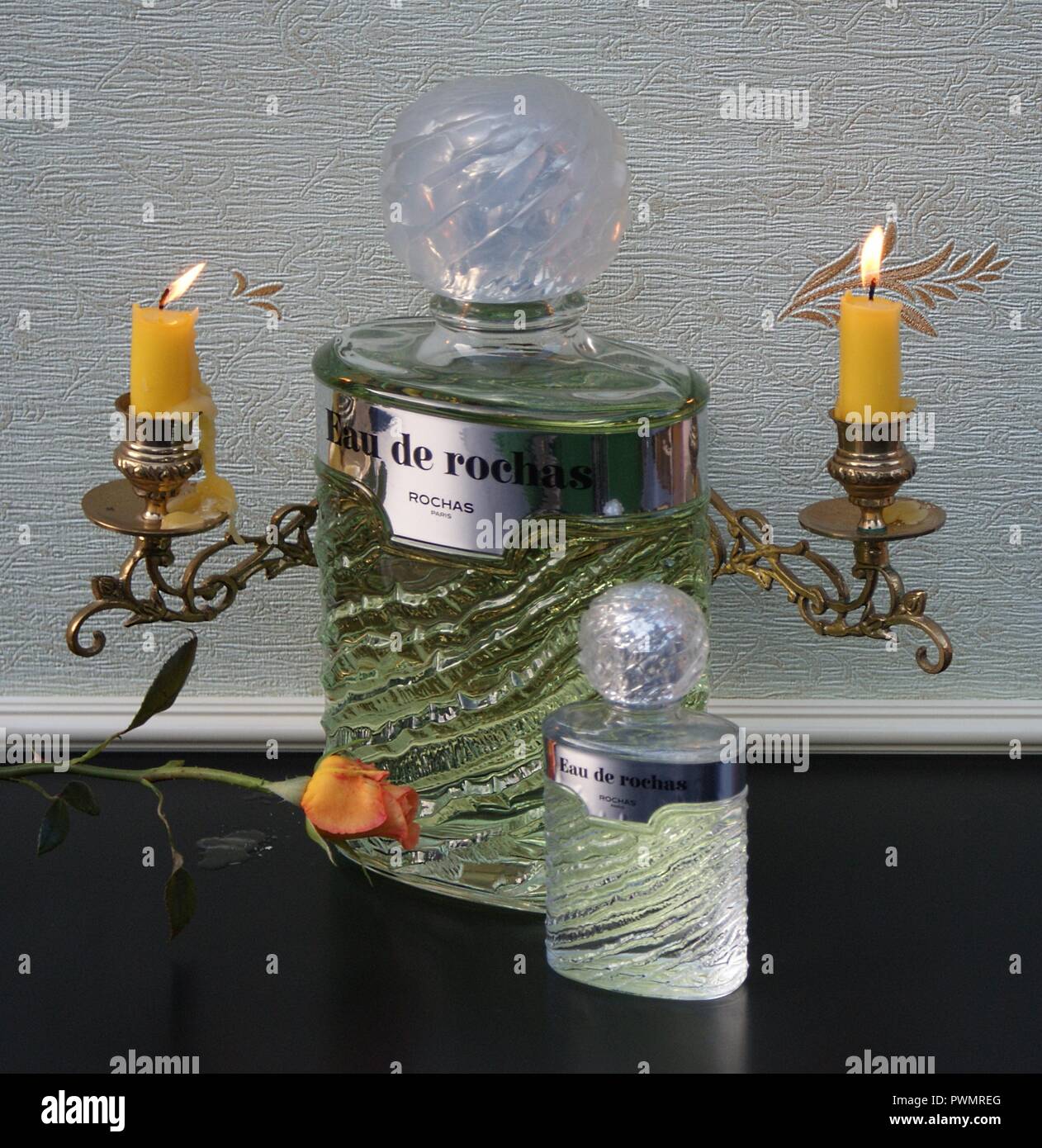 Eau de Rochas, bottiglia di profumo accanto a un profumo commerciale la  bottiglia nella parte anteriore di un pianoforte candelabri con brillanti  Candele decorata con una rosa Foto stock - Alamy