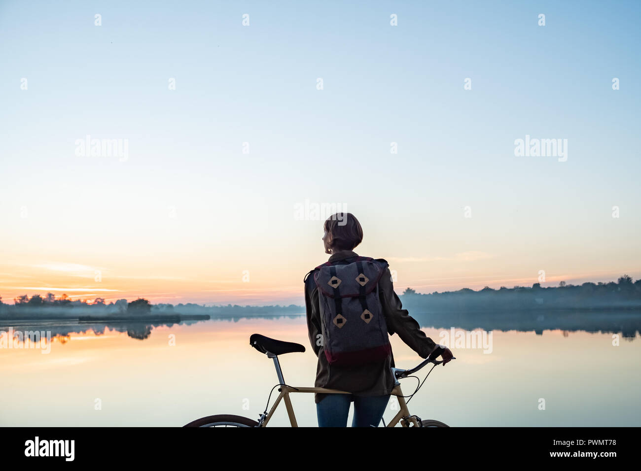 Ciclista femmina godendo di splendide blue ora scena dal lago. La donna si erge con bike e guarda al lago e al tramonto Foto Stock