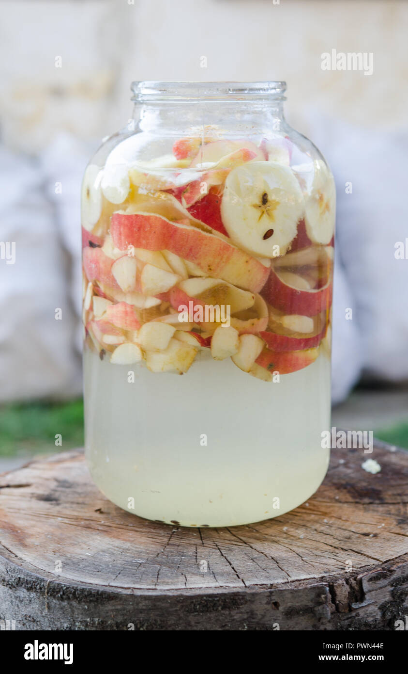 Aceto di mele rendendo - apple pezzi galleggianti in un vetro in interni in stile rustico Foto Stock