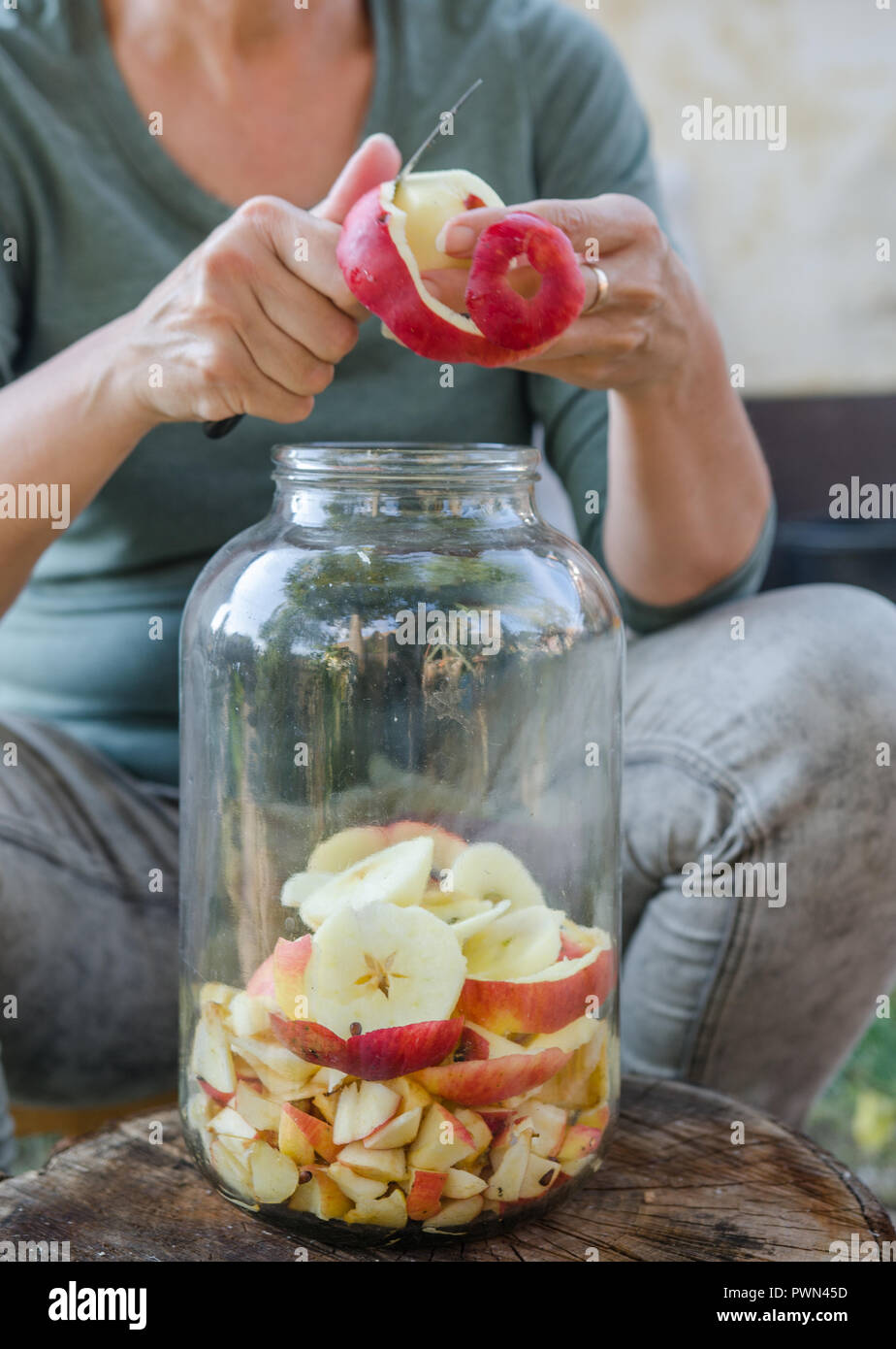 La donna fa di aceto di mele - apple peeling e tagliarla in una bottiglia Foto Stock