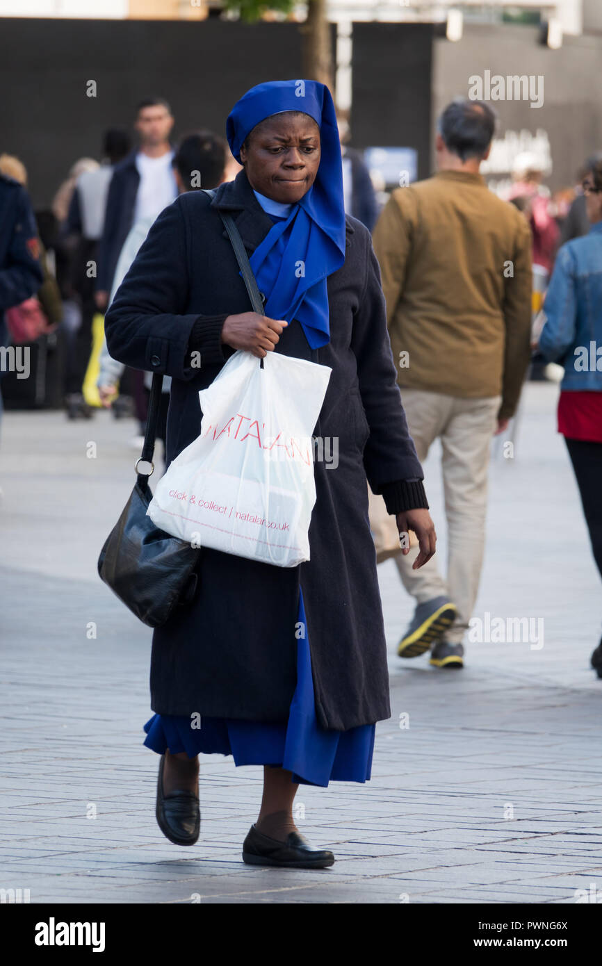 Una suora nero fuori shopping sul High St portando un sacchetto di Matalan e indossando un abito blu. Foto Stock