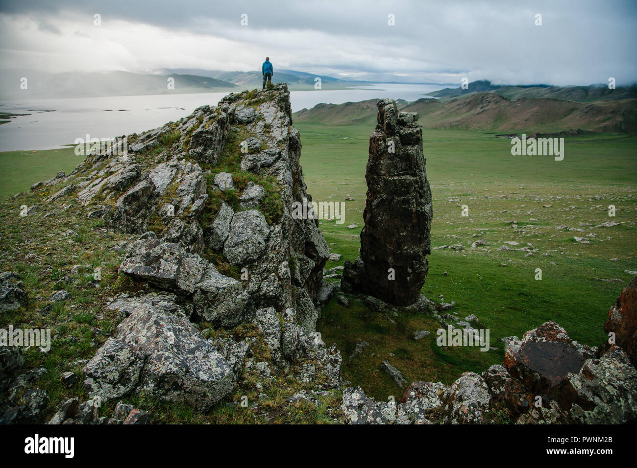 Un scalatore in piedi su una formazione di roccia guarda il paesaggio per godere la vista del Lago Bianco (Tsaagan Nuur). Tariat Arkhangai, Mongolia Foto Stock