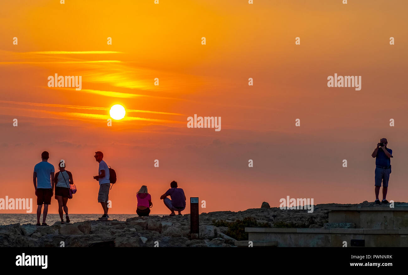 I turisti guardare il sole che tramonta al porto di Paphos, Cipro. Foto Stock