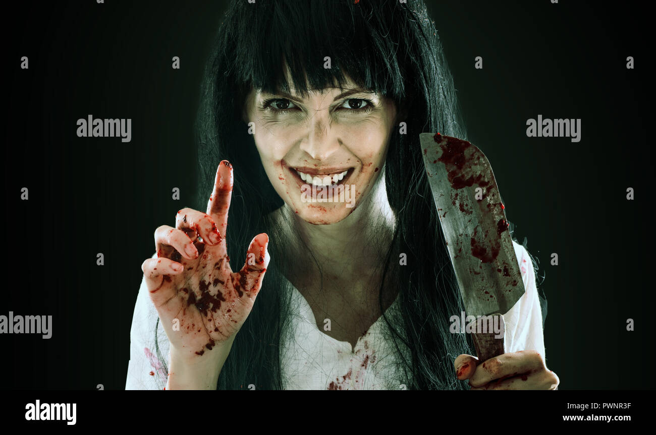 Halloween horror. Crazy sanguinosa spaventoso maniaco sorridente ragazza con il coltello macellaio cleaver rivolti a voi nella fotocamera su sfondo nero Foto Stock