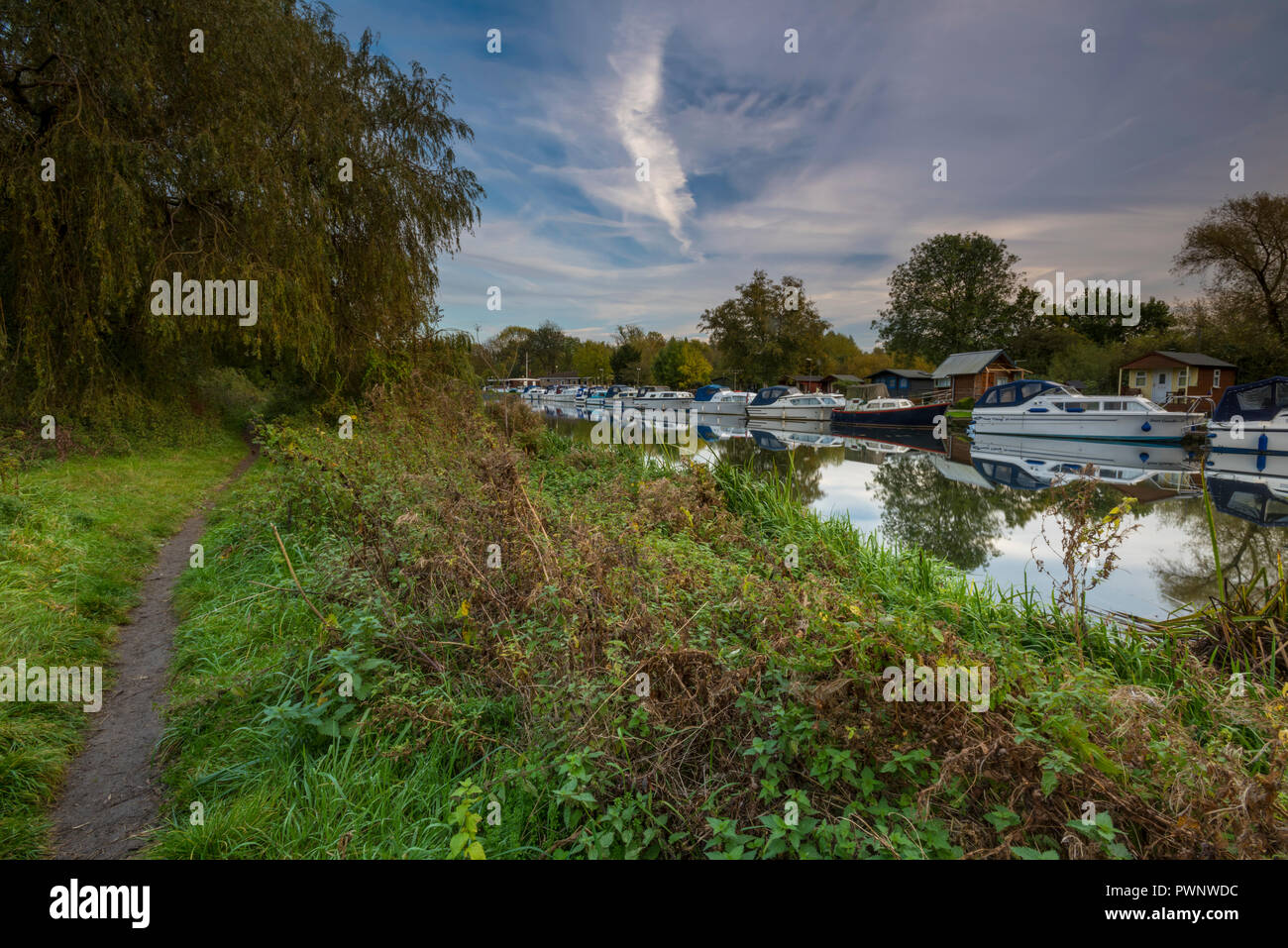 Pressione atmosferica della luce della sera sul fiume Nene a Orton vicino a Peterborough con barche ormeggiate sulla riva del fiume e un percorso lungo la riva. Foto Stock