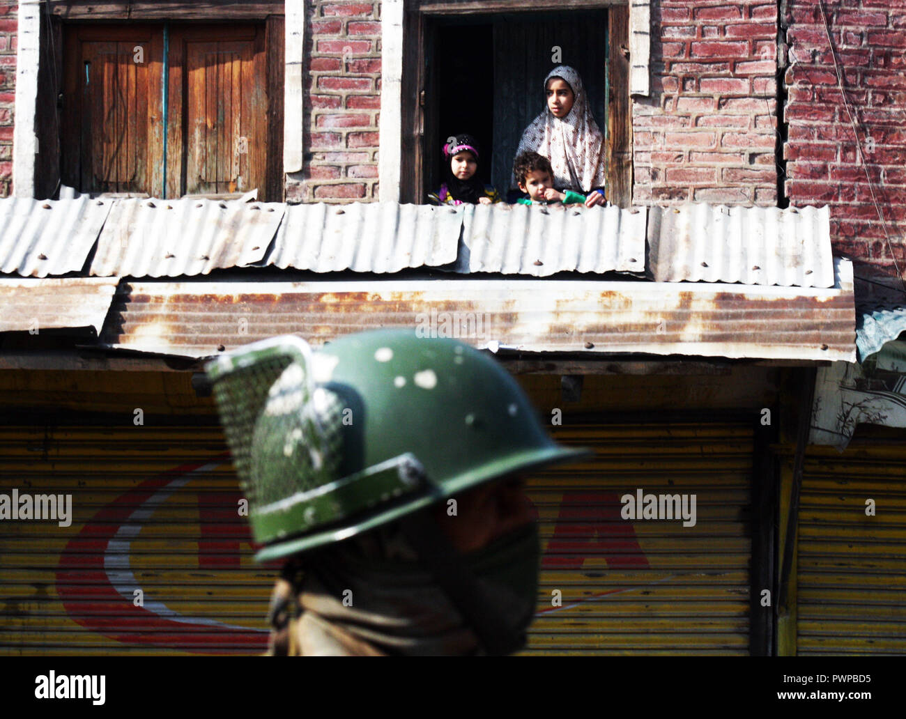 Srinagar Kashmir. 18 ott 2018. Un soldato indiano sta di guardia come figli del Kashmir guardando sulla finestra della loro casa durante il coprifuoco simili restrizioni in parti della valle .Il Giunto resistenza Leadership (JRL), un conglomerato separatista guidato da Syed Ali Geelani, Mirwaiz Umer Farooq e Muhammad Yasin Malik, chiamato l'arresto contro l'uccisione di Lashkar-e-Taiba (LET) commander,Mehrajudd in Bangroo, suo associare Faiz Ahmad Waza e Rayees Ahmad in uno scontro a fuoco il mercoledì a Srinagar's Fateh Kadal area.©Sofi Suhail/Alamy Live News Foto Stock