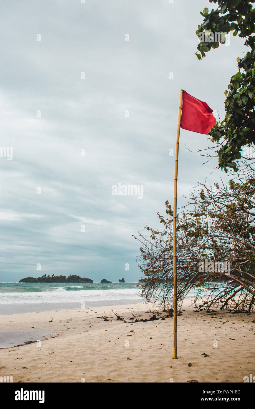 Bandiera rossa sulla ventosa di sabbia bianca di rana rossa Beach, un isola dei Caraibi al largo della costa di Panama Foto Stock