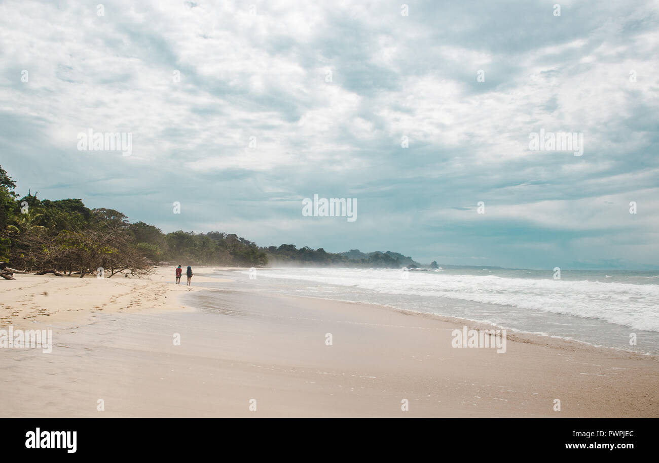 Due viaggiatori con lo zaino in spalla a piedi giù per la vasta spiaggia di sabbia bianca di rana rossa Beach, un isola dei Caraibi al largo della costa di Panama Foto Stock