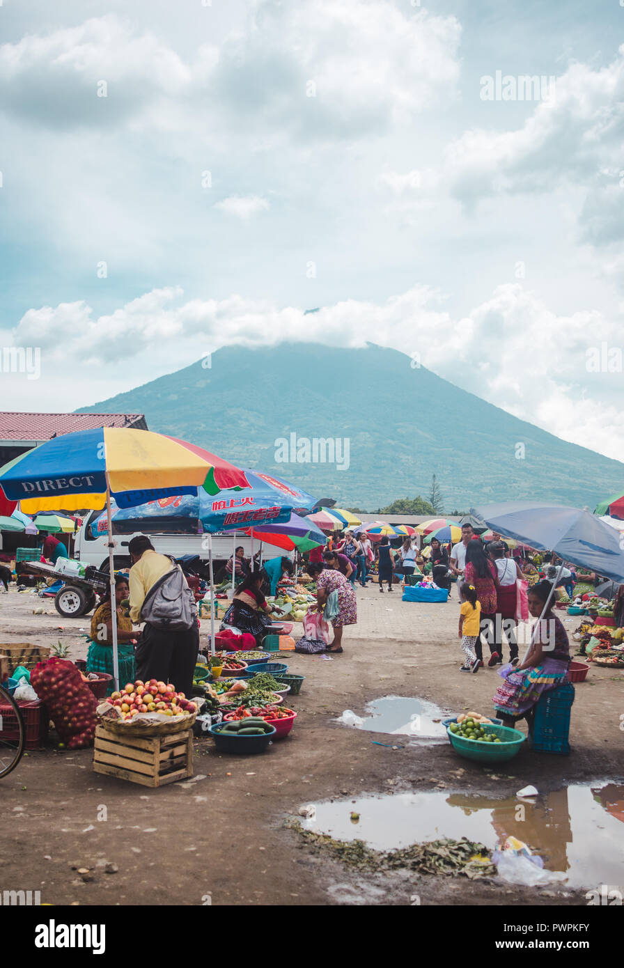 Le donne e le ragazze in tradizionale abito maya vendono frutti sotto gli ombrelli al di fuori di un mercato in Antigua, Guatemala sotto l'ombra di un vulcano Foto Stock