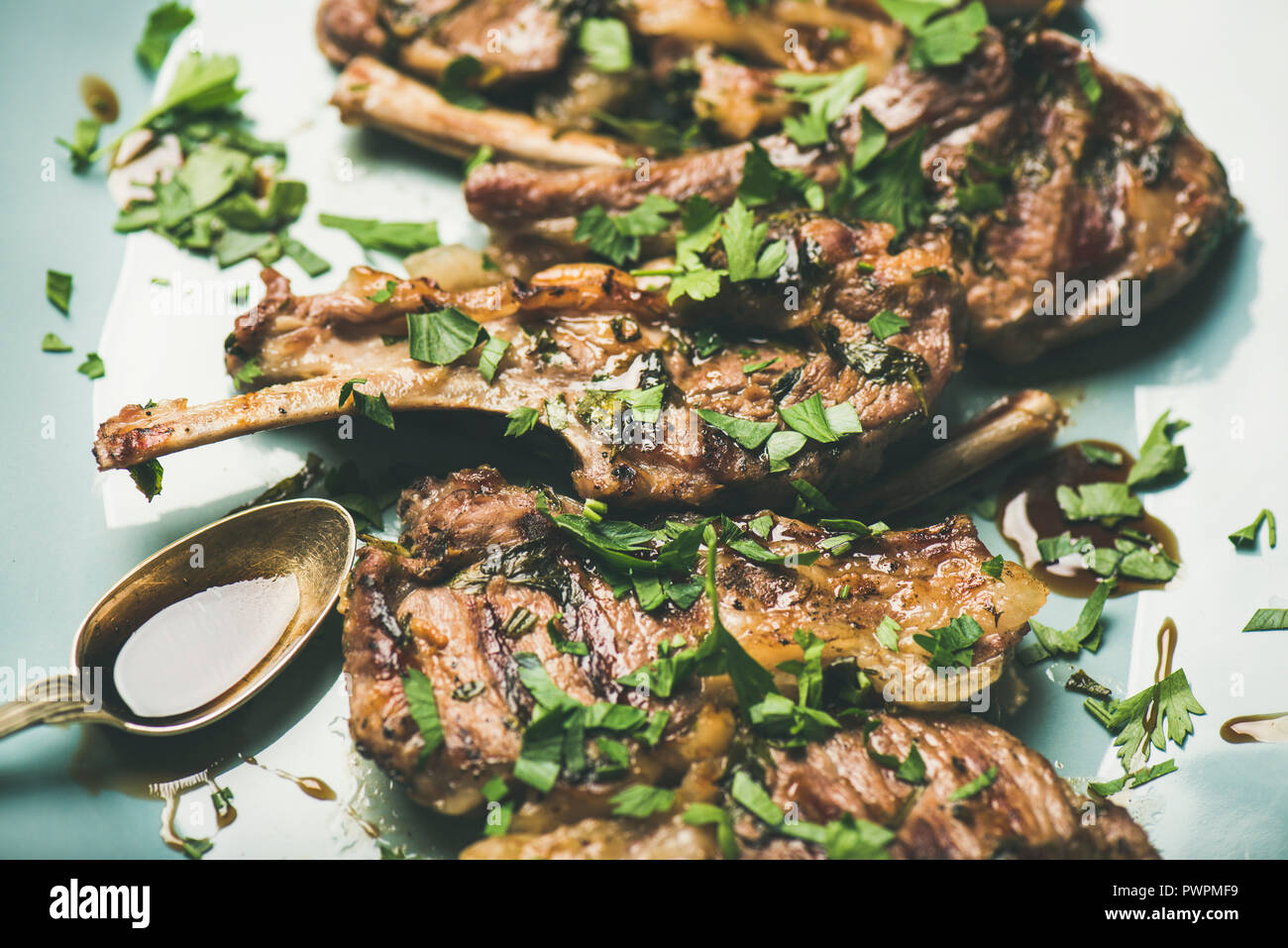 Cena a base di carne. Grigliata di costolette di agnello con prezzemolo verde e salsa in blu che serve la piastra al di sopra della tabella di calcestruzzo sfondo, il fuoco selettivo, orizzontale composit Foto Stock