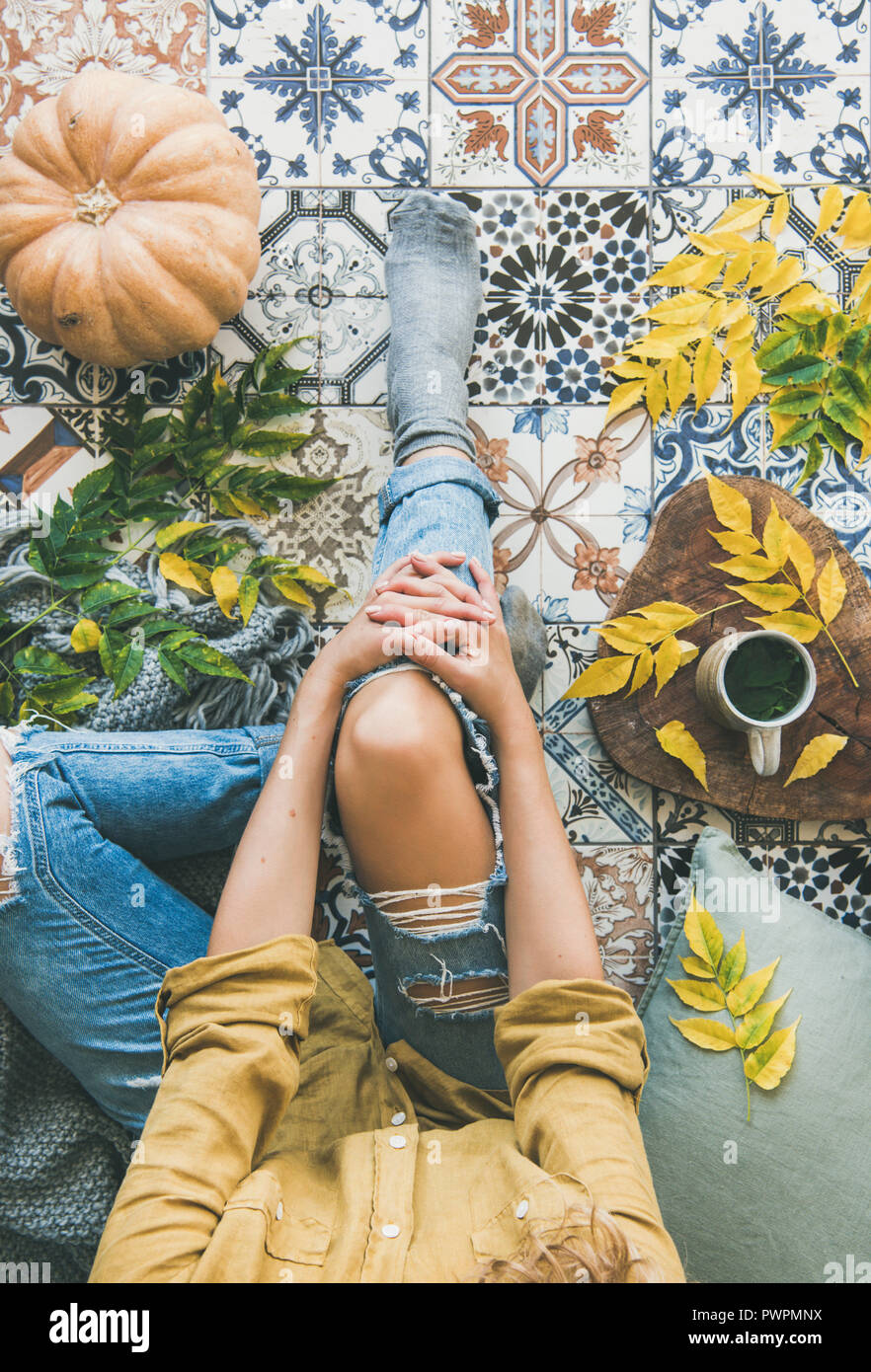 Autunno o caduta balcone tea time. Flat-lay di caduta foglie, calde coperte, la zucca e la tazza di tè alle erbe e donna seduta su colorato pavimento piastrellato, Foto Stock