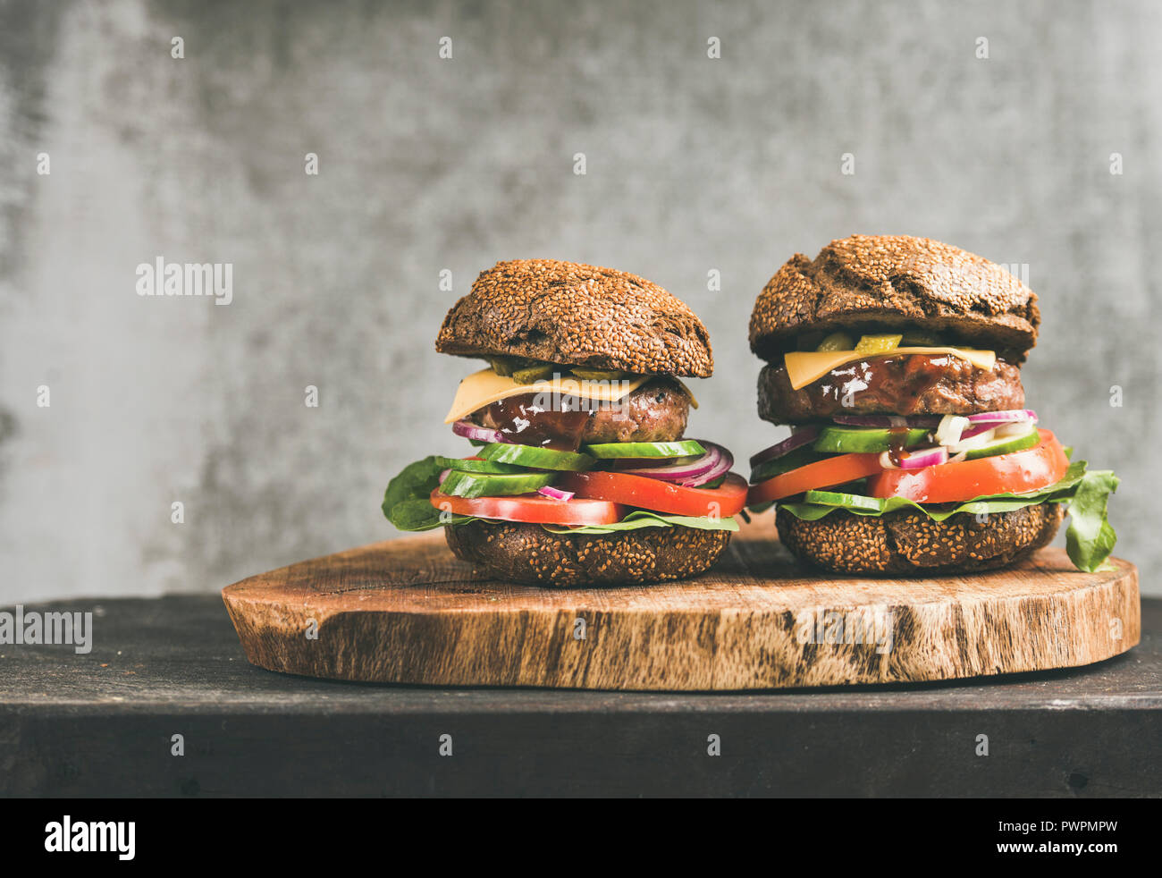 Le carni bovine cheeseburger con salsa barbecue rustico di legno, grigio muro di cemento a sfondo, copia dello spazio. Comfort food, burger bistro concept Foto Stock