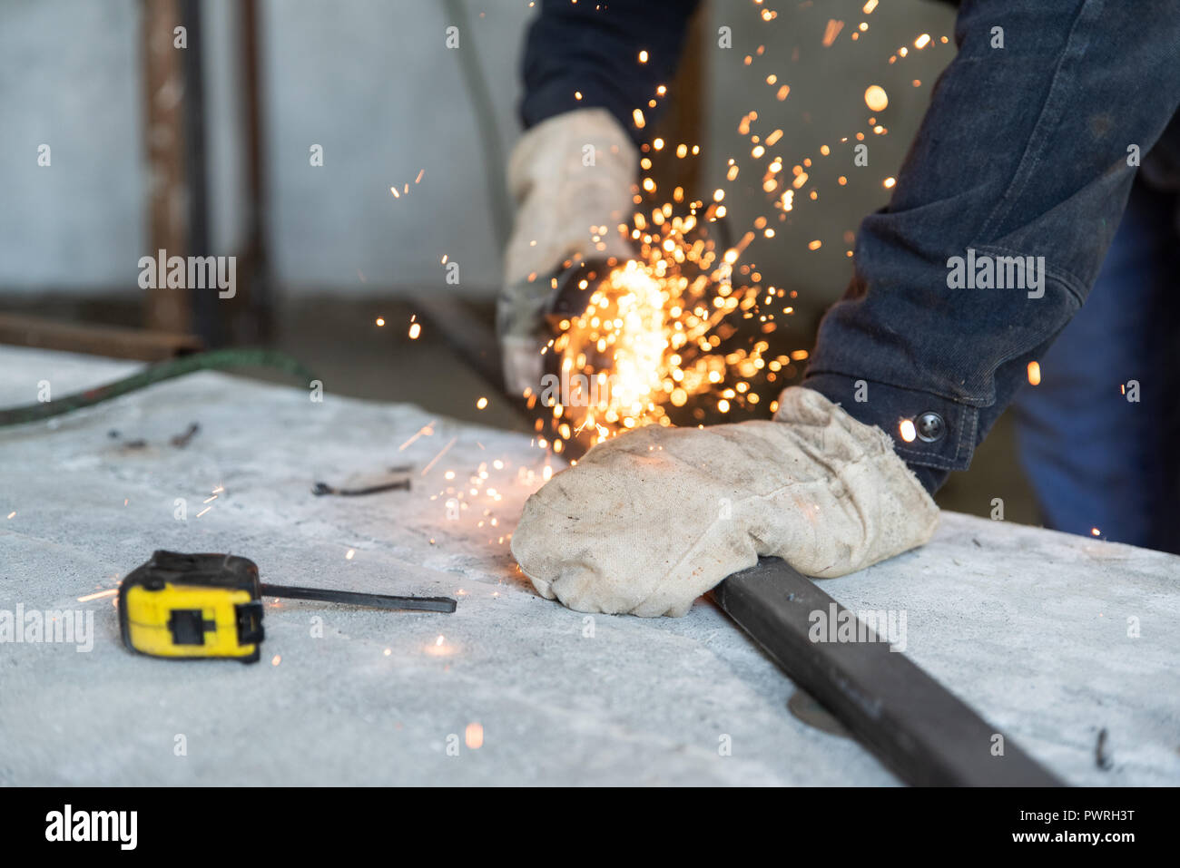 Processo di taglio del profilo metallico con angolo elettrico smerigliatrice. Preparazione dei pezzi per la saldatura di costruzioni in metallo. Persone al lavoro, professione Foto Stock