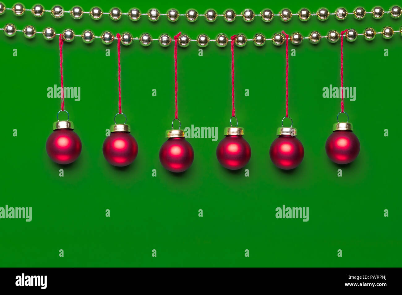 Sei piccole finitura opaca di colore rosso Natale ornamenti appeso su una riga decorata da lucido dorato perline di Natale corona su sfondo verde in stu Foto Stock