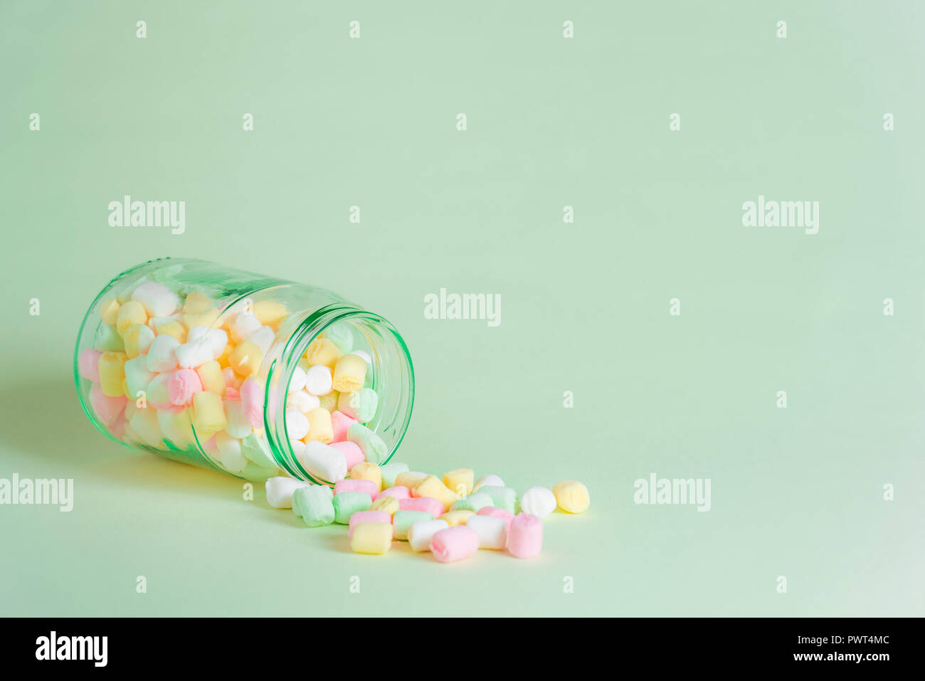 Brillante immagine minimalista con un vaso di vetro capovolto su una carta di colore verdastro sfondo, piena di minuscoli multicolore di marshmallows. American tratta d'inverno. Foto Stock