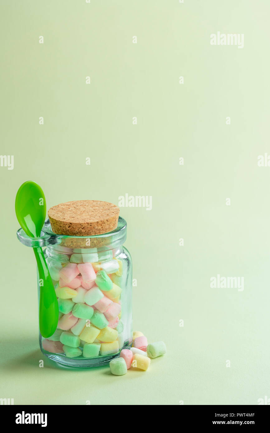 Immagine di dimensione ridotta con una bottiglia di vetro piena di colori vari tiny marshmallows e un cucchiaio di verde ad esso collegato, su una carta di colore verdastro sfondo. Foto Stock