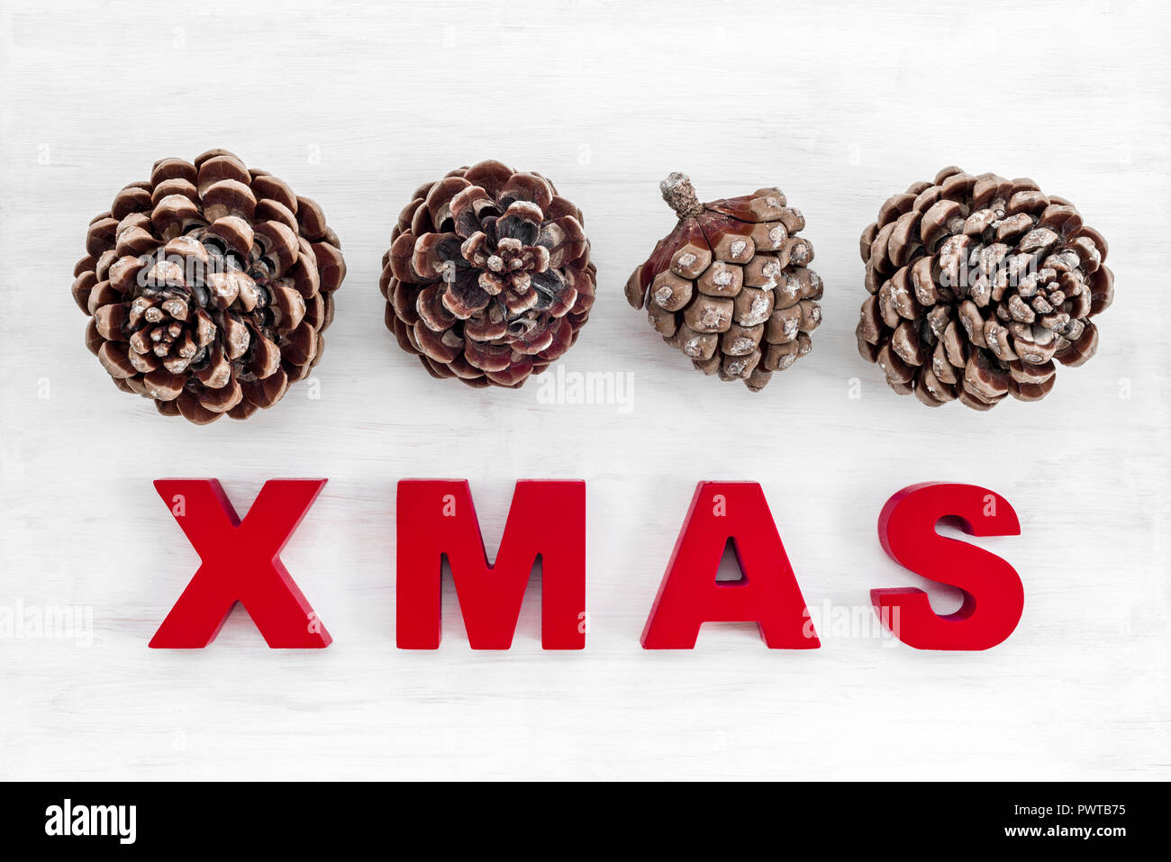 Tema Natale. Pino coni e la parola Xmas scritto in lettere rosse sul bianco sullo sfondo di legno. Foto Stock