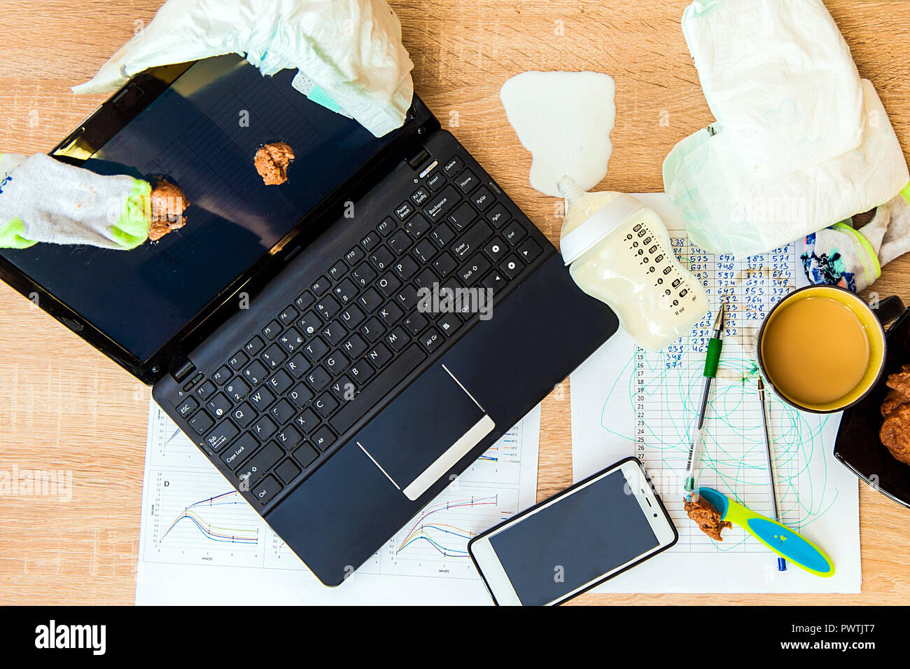 Un concetto di immagine per aver baby e lavora da casa. Posto di lavoro disordinati, pannolino, crema di farina e di latte per un bambino sullo schermo, latte versato. Foto Stock