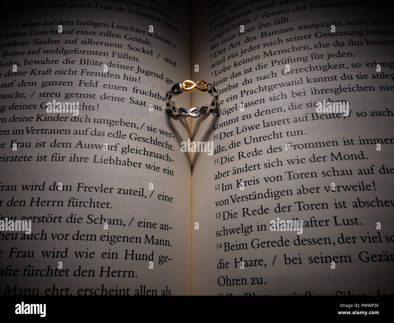 Un anello d'oro posto su un libro che ha reso un ombra nella forma di un cuore. L'anello con il simbolo di infinito è posto su una Sacra Bibbia. Foto Stock