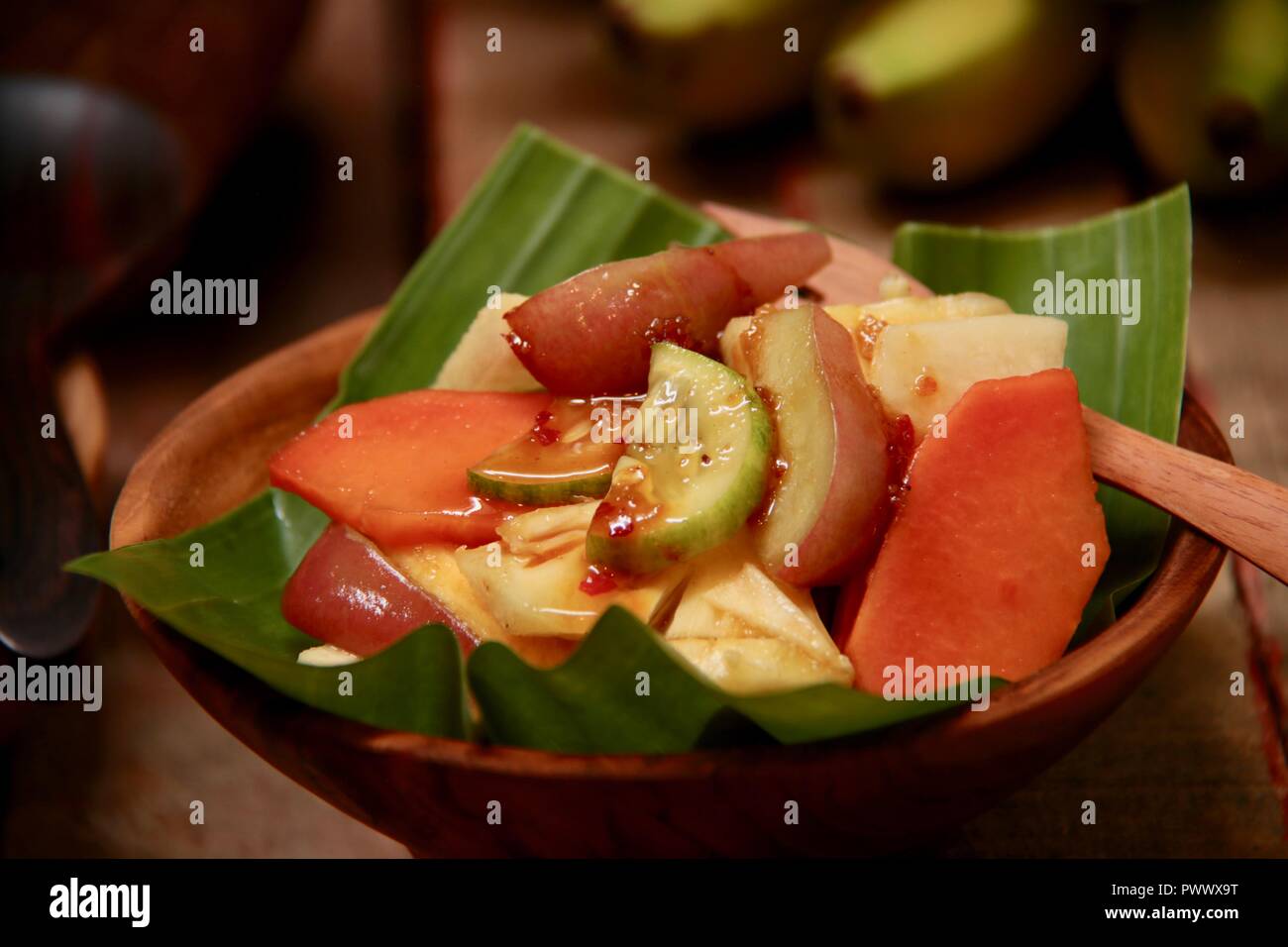 Rujak buah una, indonesiano insalata di frutta con il piccante lo zucchero di cocco medicazione. Placcato su un poco profondo la ciotola di legno rivestita con foglia di banano, Foto Stock
