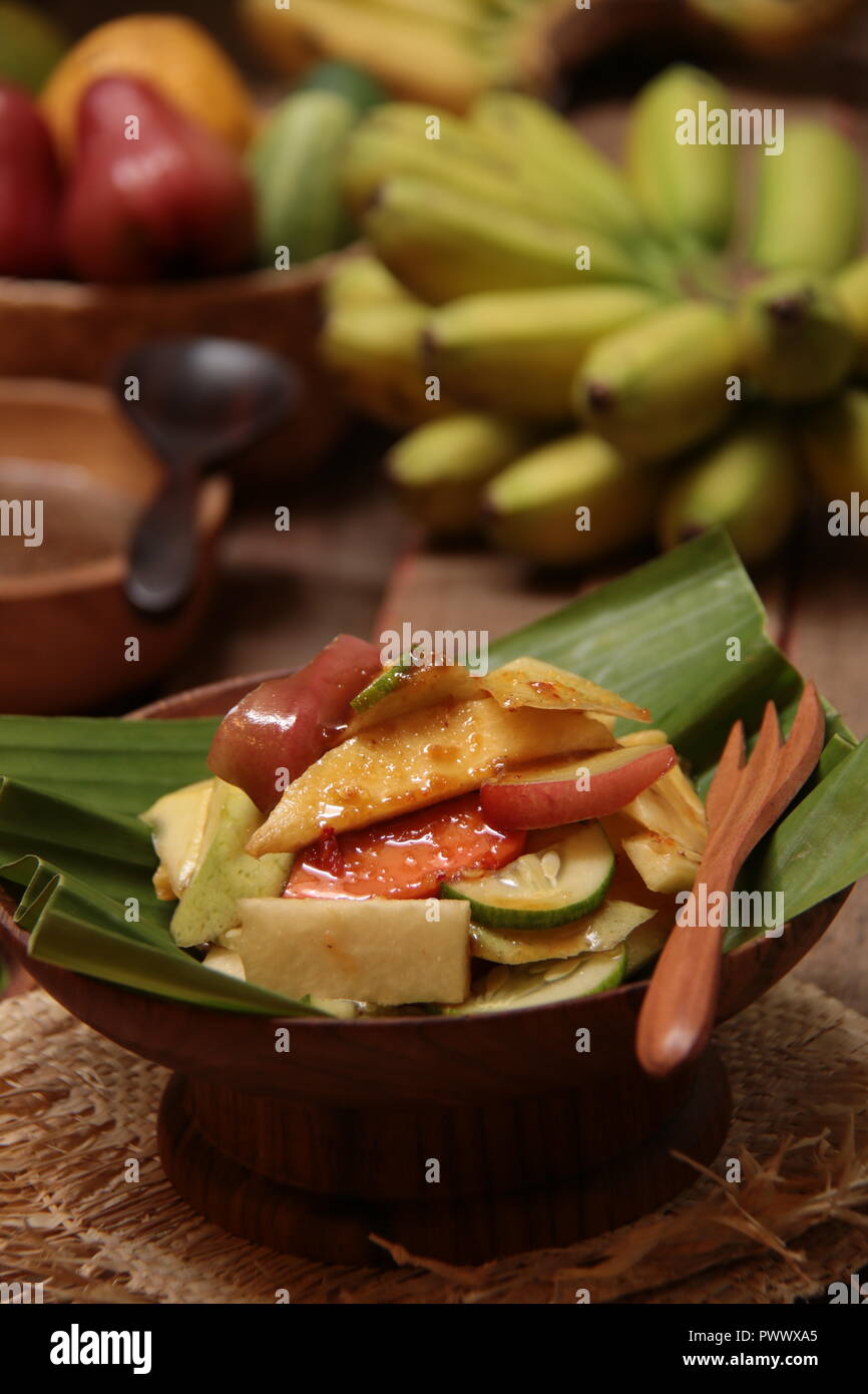 Rujak buah una, indonesiano insalata di frutta con il piccante lo zucchero di cocco medicazione. Placcato su un poco profondo la ciotola di legno rivestita con foglia di banano, Foto Stock