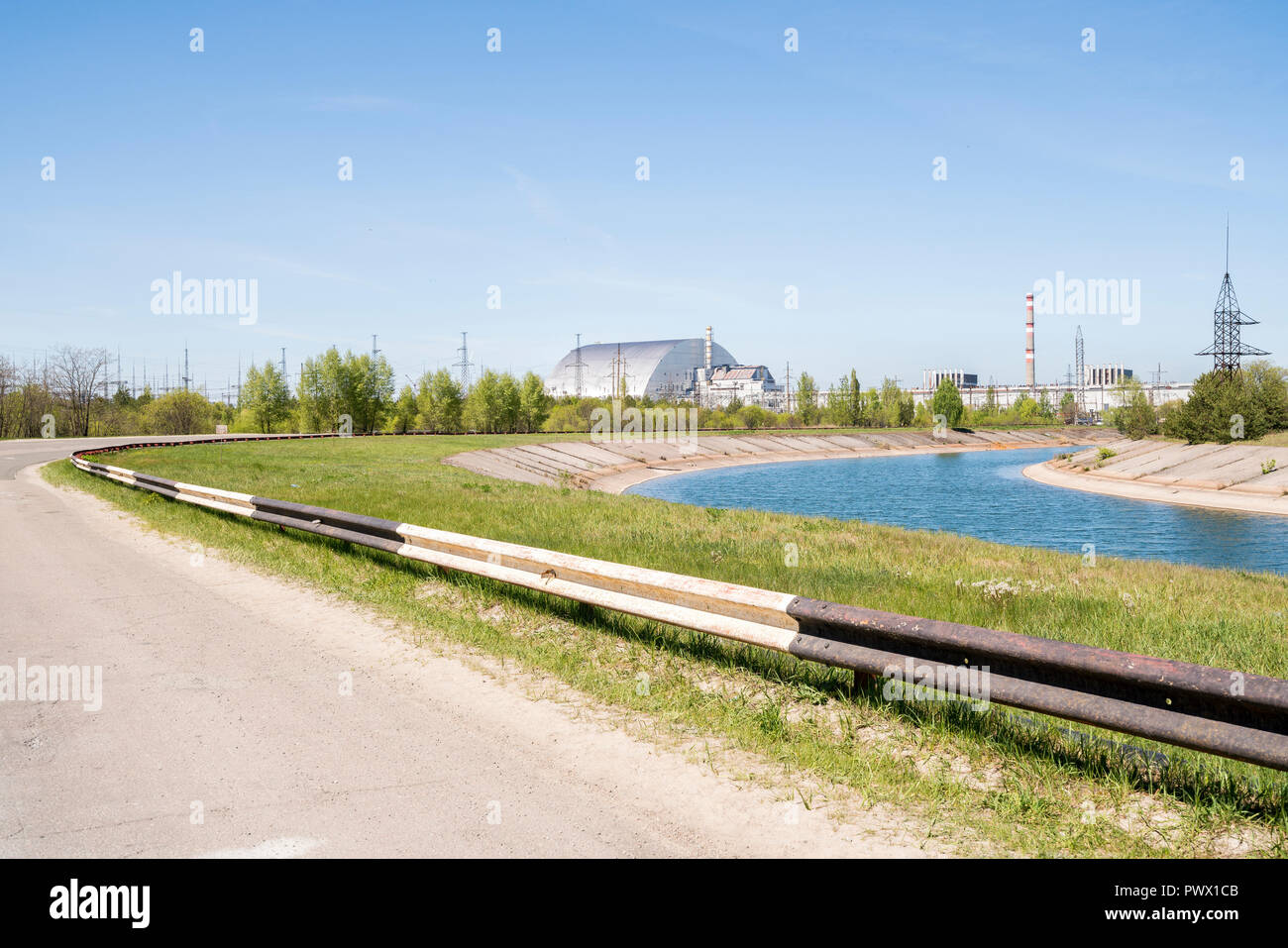 Vista lungo una strada rurale verso Chernobyl, in Ucraina, in acciaio massiccio e struttura in calcestruzzo che ricopre il reattore nucleare n. 4 nella distanza. Foto Stock