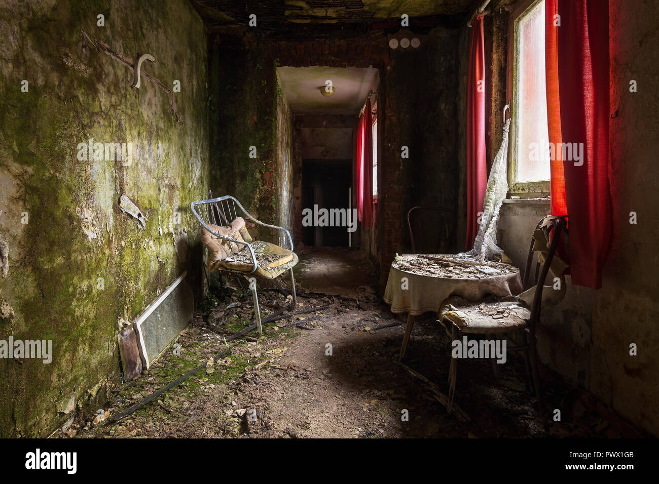 Vista interna di un corridoio buio con sedie e tendaggi rossi in un hotel abbandonato in Germania. Foto Stock
