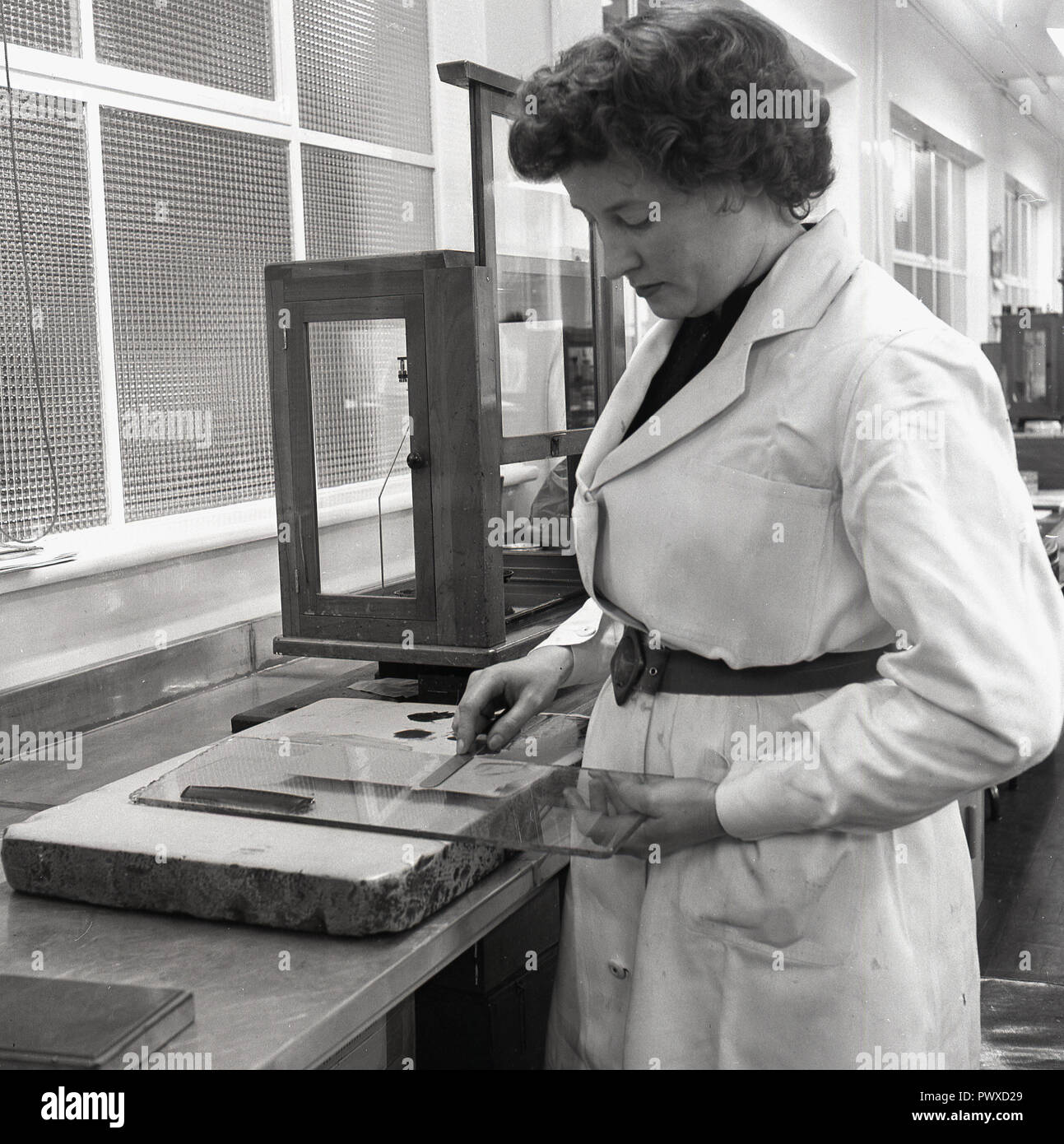 Degli anni Cinquanta, storico, fabbricazione di vernice, un tecnico femmina indossando un white-coat in corrispondenza di un banco di lavoro tenendo un vetro dello schermo e lama di miscelazione, Inghilterra, Regno Unito. Foto Stock