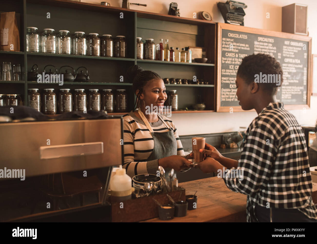 Sorridente African barista consegna a un cliente il suo drink fine Foto Stock