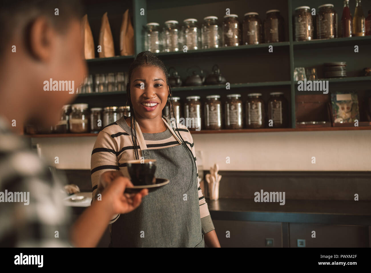 Sorridente giovane africana barista dando il suo cliente un cappuccino Foto Stock