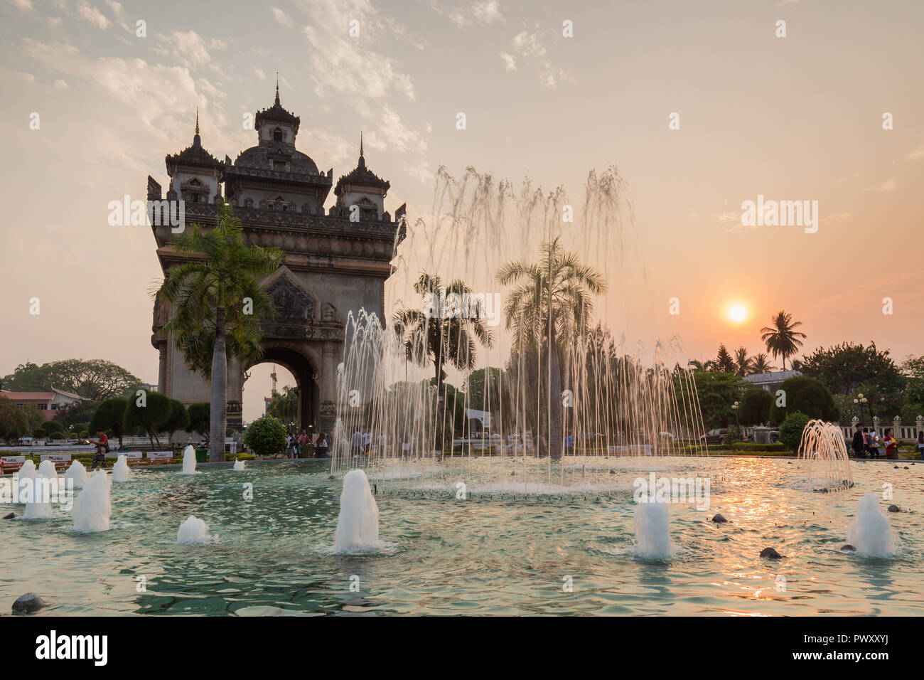 Fontana, palme, turisti e gente locale presso il Patuxai (Patuxay), vittoria gate o gate del trionfo, monumento di guerra in Vientiane, Laos, al tramonto. Foto Stock