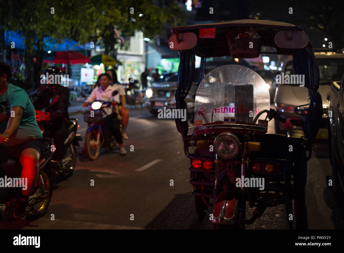 Parcheggiato a tre ruote taxi chiamato jumbo (o un tuk-tuk), automobili e poche persone in scooter sul Quai Fa Ngum Road a Vientiane, Laos, di notte. Foto Stock