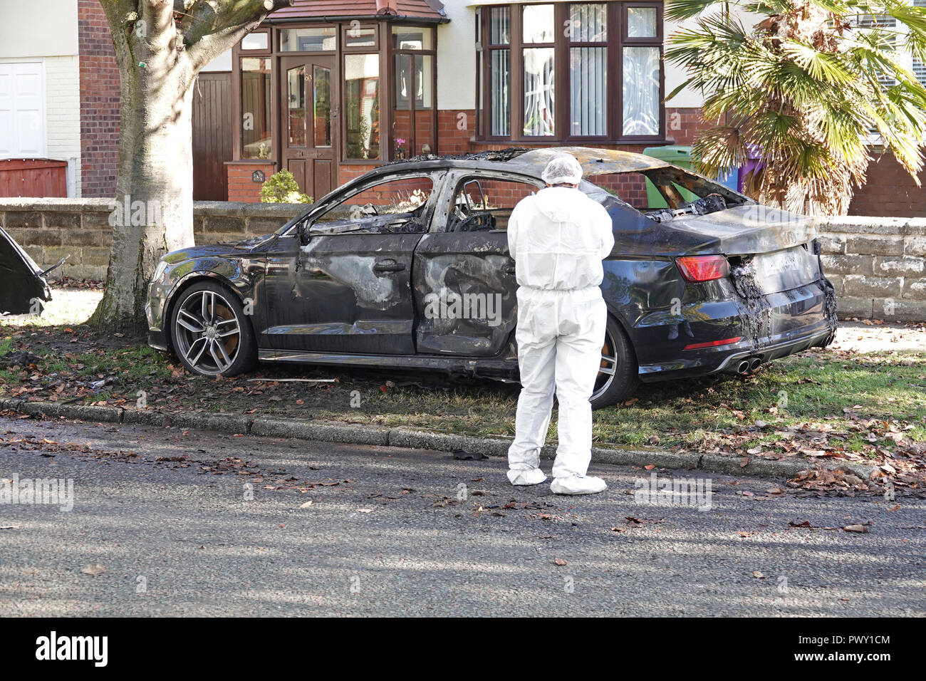 Liverpool, Regno Unito. Il 18 ottobre 2018. Un cordone di polizia attorno ad un bruciato auto in strada Abbeystead Childwall. Un colore scuro Audi abbandonate su un orlo di erba, 1.7 miglia da ultima notte di riprese in Alderson Rd, Wavertree. Un forensics officer è di scattare foto e la raccolta delle prove sulla scena. La polizia non sono dicendo in questa fase se la vettura è stata coinvolta in ultima notte di omicidio. Credito: Ken Biggs/Alamy Live News. Foto Stock