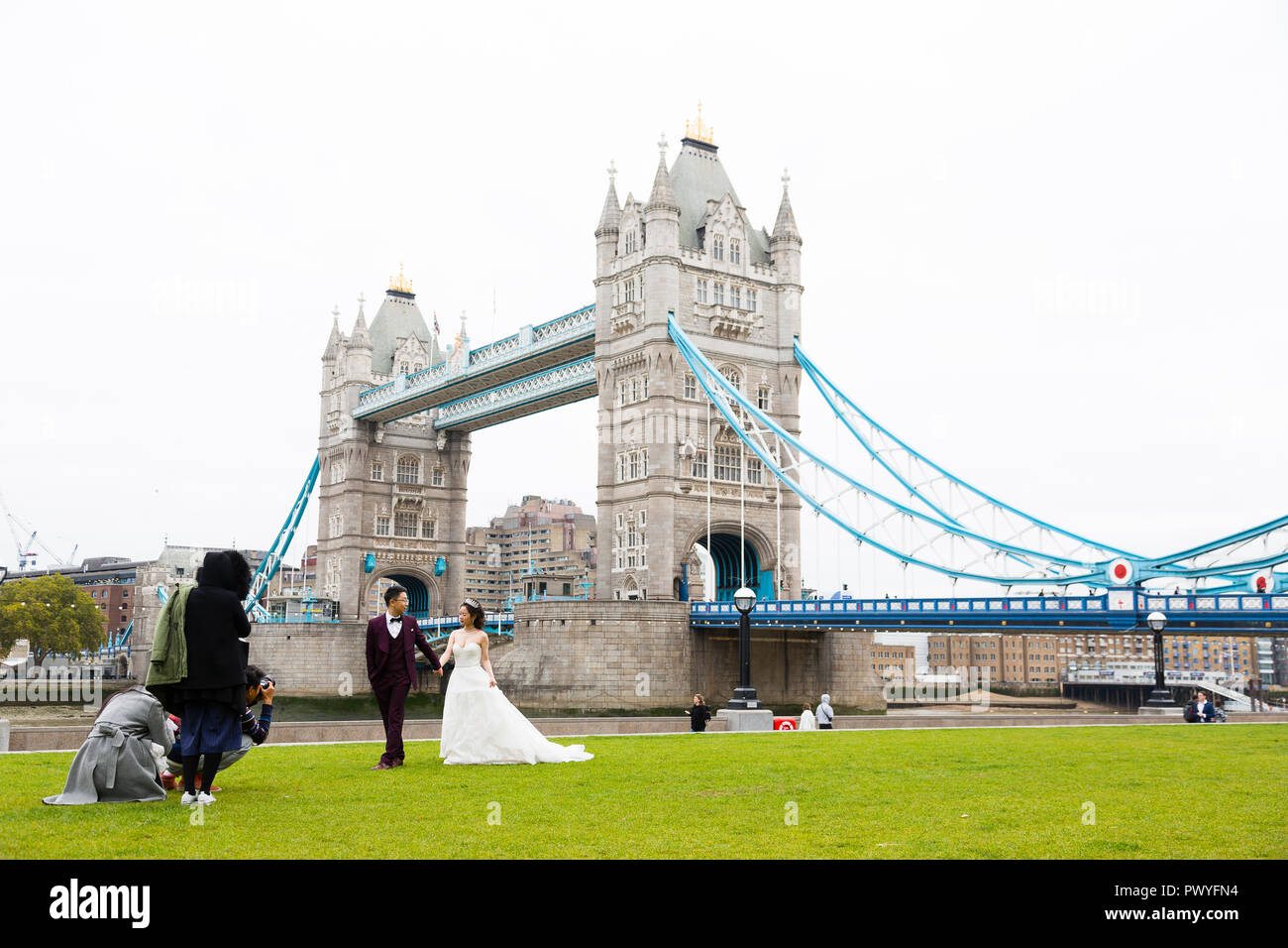 Londra, Regno Unito. Un fotografo professionista si accovaccia sul terreno per scattare una foto di un asiatico giovane nella parte anteriore del Tower Bridge. Foto Stock